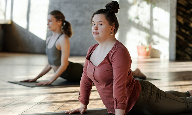 Two woman, one with Down's Syndrome, doing yoga on mats in a gym