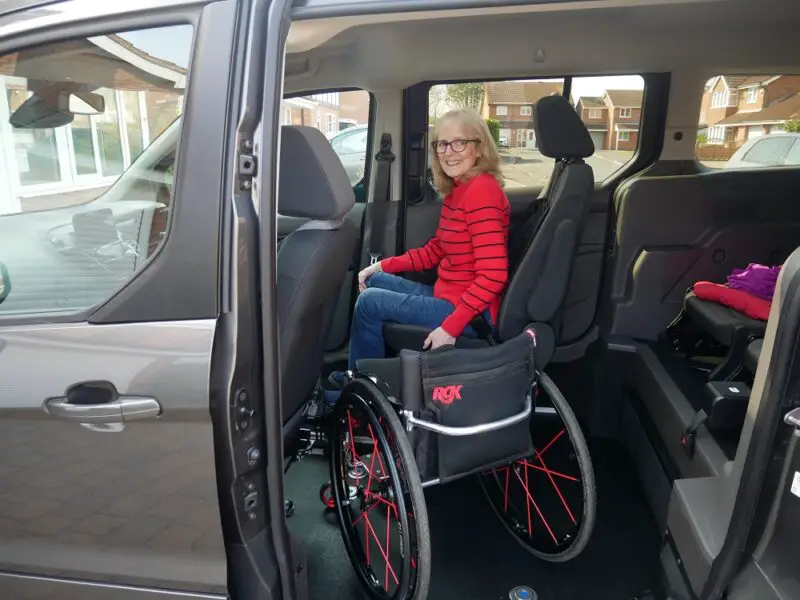 Wheelchair user Susan wearing a black and red top having just transferred from her wheelchair into the driver's seat of her Sirus Ford Grand Tourneo Connect wheelchair accessible vehicle