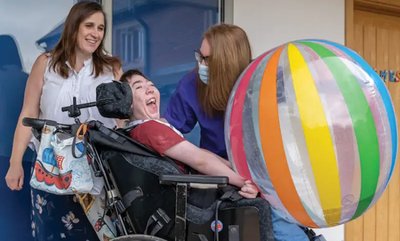 Skiggle Co-founders Christine and Helen with James who is sat in his wheelchair smiling with a large beach ball on his lap