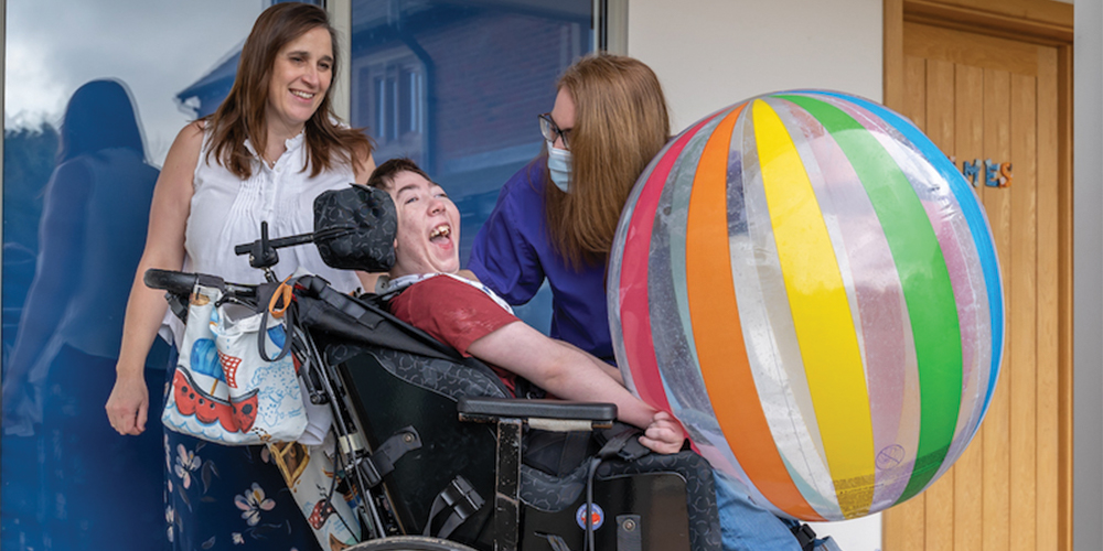 Skiggle Co-founders Christine and Helen with James who is sat in his wheelchair smiling with a large beach ball on his lap