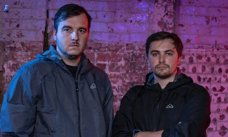 Deaf contestants James and Nathan on Hunted standing wearing grey and black jackets in front of a wall