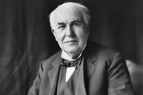 A black and white close up image of Thomas Edison in a black suit with black bowtie and short white hair