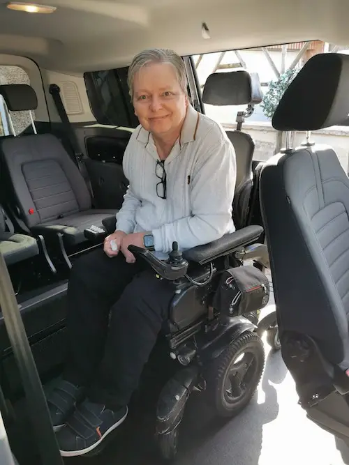 Mark with short grey hair, a pale blue jumper and navy trousers sat in his power wheelchair in the back of his Sirus wheelchair accessible vehicle having driven up the ramp at the side to get into the car