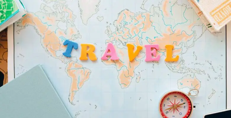 Travel image showing the words travel spelt out in yellow, blue and pink letters on a map of the world with a compass and notebooks