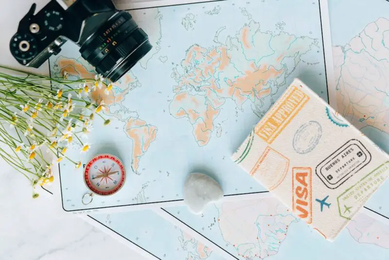 A world map on a table with a camera, passport cover, compass and flowers on it
