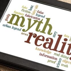 Myths and reality written in green and red on a tablet lying on a table next to a white cup of coffee and a stylus. There are other words around myth and reality, including logic, fiction, information, proof and false