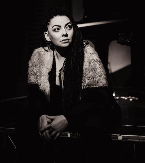 Black and white portrait of pianist Ruth McGinley. She sits and looks off to the right of the camera. Her hair is pulled back on one side and she wears a fur cardigan.