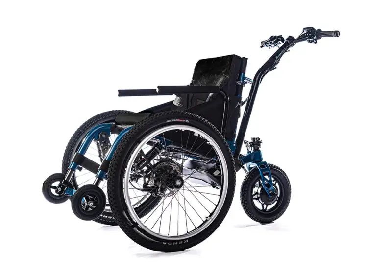 The Mountain Trike MT ePush all-terrain wheelchair with two large front wheels, two smaller back wheels and two additional small wheels up high at the front. The seat is black and cushioned and the metal is blue. There is a bar with handles at the back.