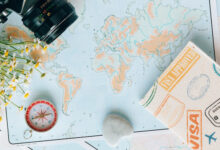 A world map laid out on a table with a camera in the top right corner and a compass and passport cover