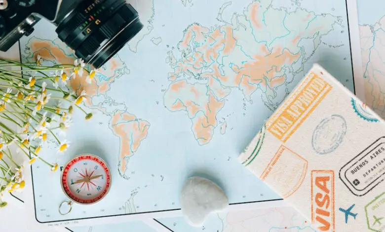 A world map laid out on a table with a camera in the top right corner and a compass and passport cover