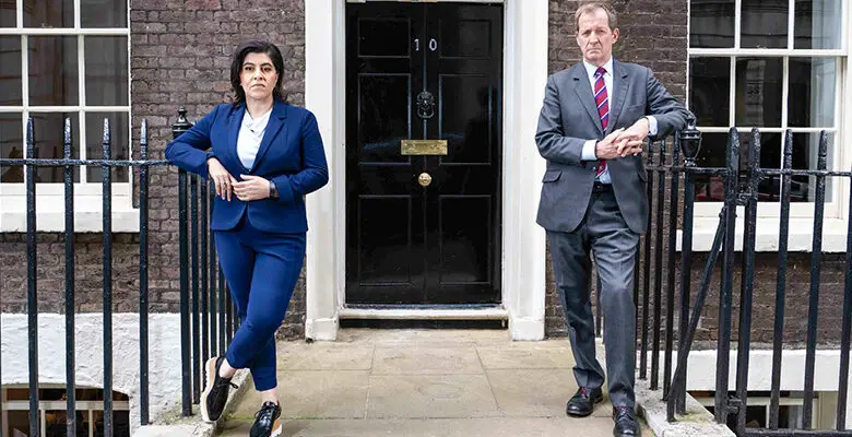 Baroness Sayeeda Wars in a blue suit with Alastair Campbell in a grey suit stood either side of the No 10 Downing Street door for Make Me Prime Minister