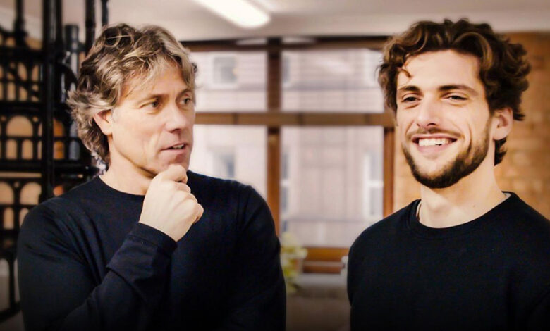 John Bishop with deaf son Joe. They both have dark curly hair and are wearing black jumpers. Joe is smiling and has a beard.