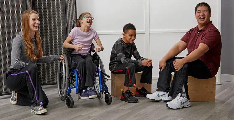 Four people - two children (a boy and girl) and two adults (a man and women) - wearing BeFree ZipOn adaptive trousers sitting and kneeling smiling at the camera