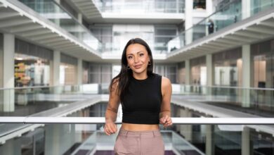 Natalie is a women of mixed heritage. She is standing inside at the Channel 4 offices with her elbows on the banister going across. Natalie is wearing a black crop top with beige trousers
