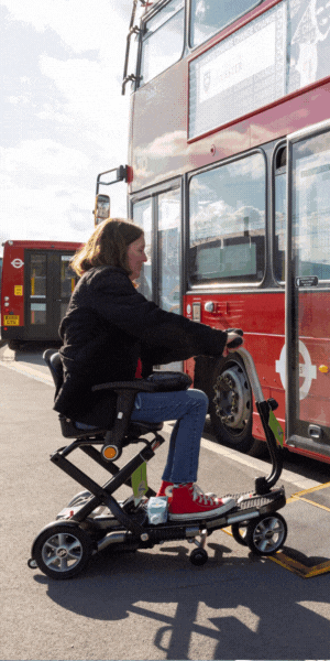 An image of a woman with long brown hair wearing a black jacket and blue jeans on a mobility scooter getting onto a London bus using a ramp. Words on the screen read: 'Have your say on possible new and extended bus routes in London.' and 'TfL wants to ensure they're accessible to all.,