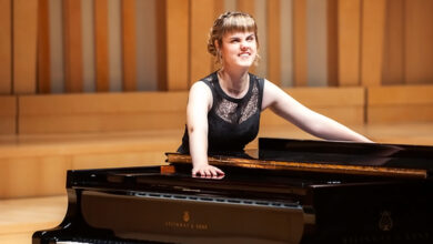 Rachel Starrit in evening attire, leaning casually on a grand piano on stage