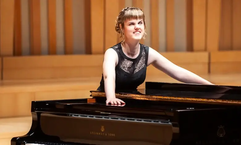 Rachel Starrit in evening attire, leaning casually on a grand piano on stage