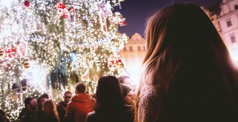 A queue of people waiting to see a tall Christmas tree covered in lights and decorations