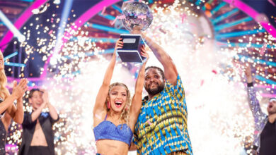 Hamza Yassin and Jowita Przystal lifting the Strictly glitterball. They are wearing brightly coloured blue and yellow outfits that they performed in for their Couple's Choice, an Afrobeats-inspired dance. There are fireworks behind them.