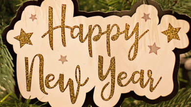 The words Happy New Year in glittery gold on a wooden board in front of a Christmas tree