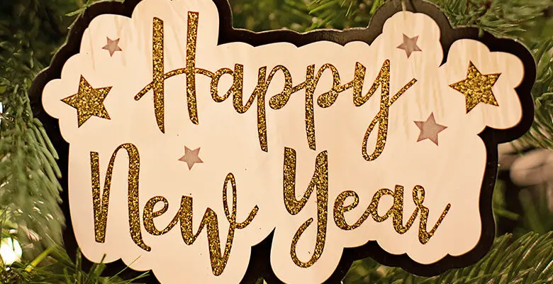 The words Happy New Year in glittery gold on a wooden board in front of a Christmas tree