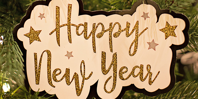 The words Happy New Year in glittery gold on a wooden board in front of a Christmas tree