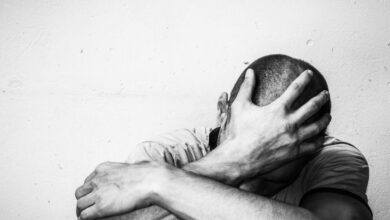 Black and white image of homeless man sitting alone on the street with his arm over his knee and his hand over his face