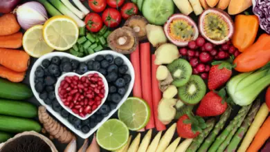 Lots of fruits and vegetables laid out with bluberries and pomegranate seeds in two white heart-shaped bowls in the middle