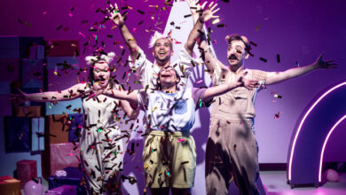 A group of actors on the stage with ticker tape and a purple background.
