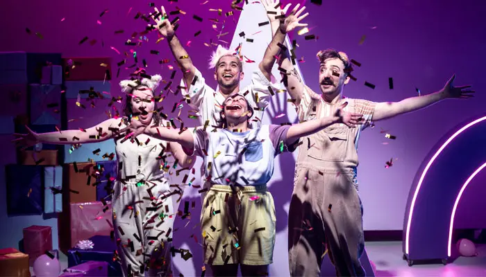 A group of actors on the stage with ticker tape and a purple background.