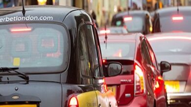 A black taxi in a queue behind a red car