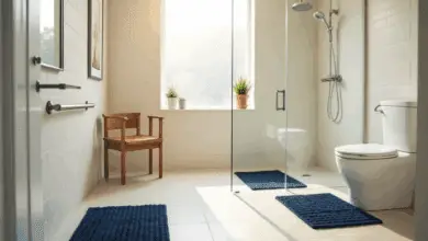 Accessible bathroom with grab bars, a walk-in shower with handheld showerhead, non-slip navy mats, a wooden shower chair, and a raised toilet.
