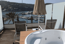Empty hot tub on a balcony overlooking a marina with yachts, hills, and palm trees in the background.