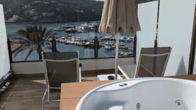 Empty hot tub on a balcony overlooking a marina with yachts, hills, and palm trees in the background.