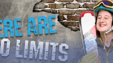 Smiling skier in a helmet and goggles holds skis beside large text on a brick wall that reads: “There Are No Limits.”
