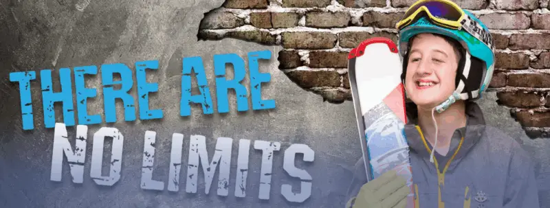 Smiling skier in a helmet and goggles holds skis beside large text on a brick wall that reads: “There Are No Limits.”