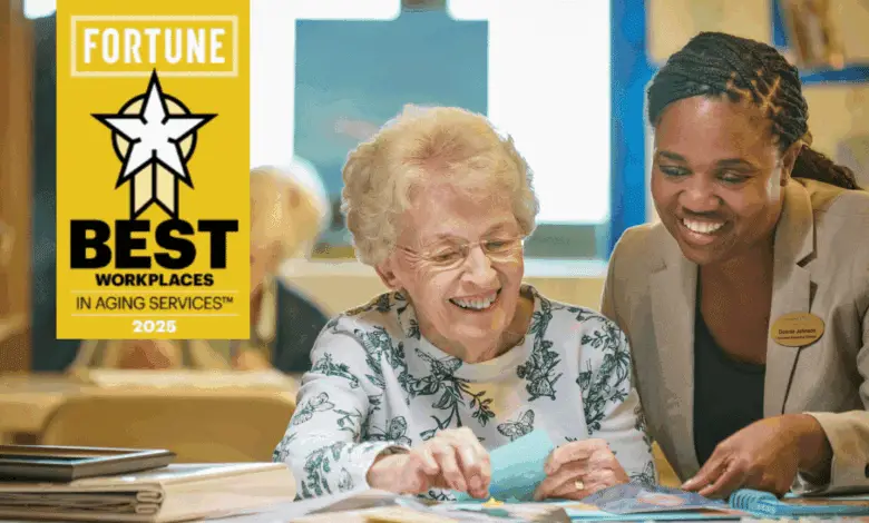 A staff member sits beside an older woman at a table, both smiling as they look at papers together. A yellow graphic reads “Fortune Best Workplaces in Aging Services 2025.”