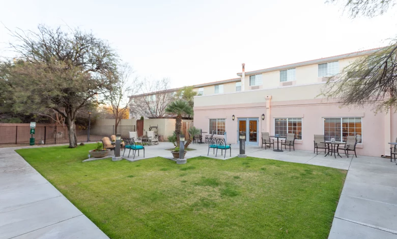 Secure outdoor courtyard at Avista Tucson with level concrete paths, green lawn, patio seating, and shaded areas beside a two-storey residential building.