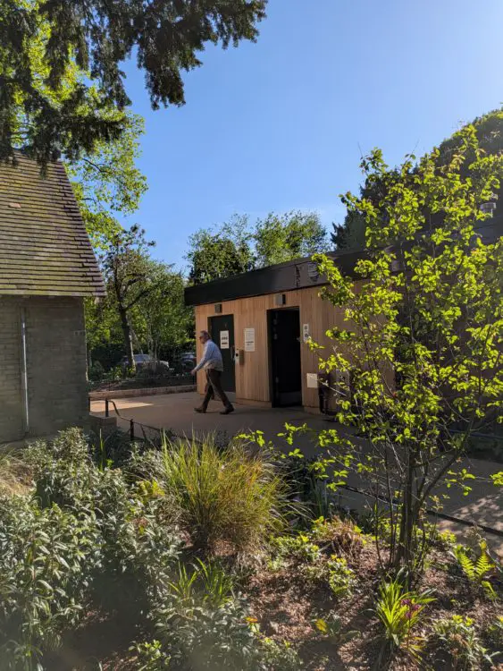 **Alt text:** Path leads to a Changing Places toilet building in Regent’s Park, set beside planting near a café. 