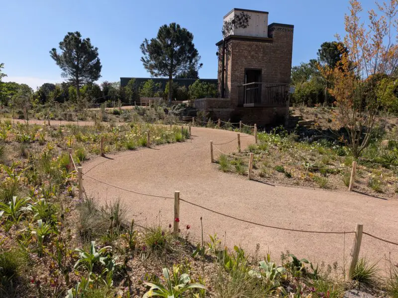 Wide, step-free path curves through planting towards an accessible brick water tower with a viewing platform