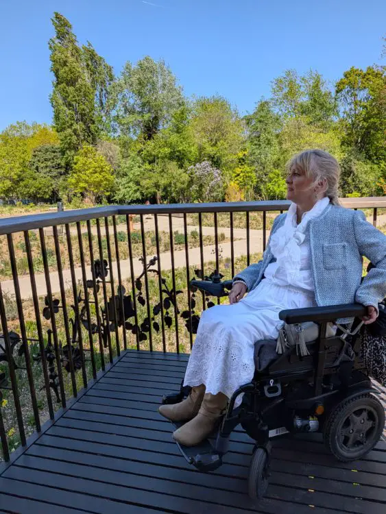 Wheelchair user sits on an accessible balcony overlooking the garden, with wide paths and planting below.