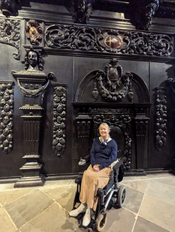 Wheelchair user seated inside Durham Cathedral in front of ornate carved woodwork and stone floors.