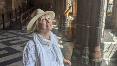 Wheelchair user in a sun hat looks up at the vaulted stone ceiling inside a cool medieval cathedral.