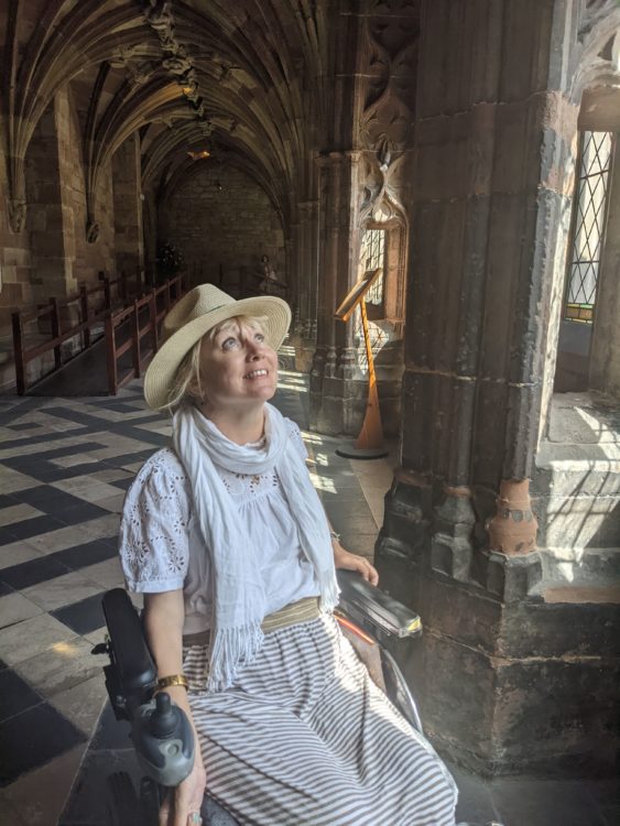 Wheelchair user in a sun hat looks up at the vaulted stone ceiling inside a cool medieval cathedral.