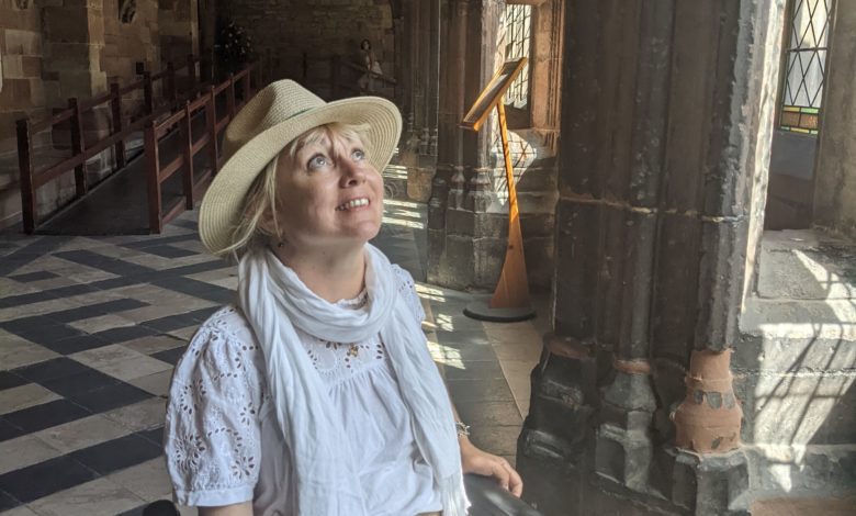 Wheelchair user in a sun hat looks up at the vaulted stone ceiling inside a cool medieval cathedral.