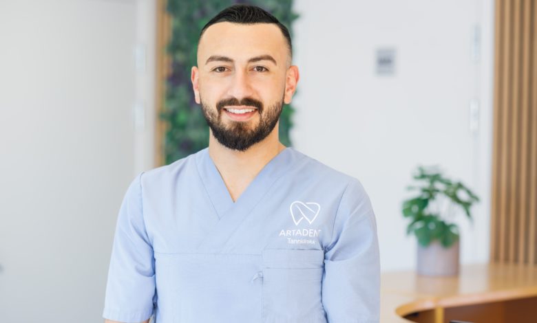 Smiling dental professional in clinic uniform standing in a modern dental practice reception area.