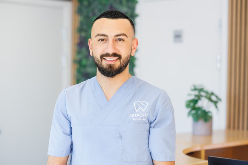 Smiling dental professional in clinic uniform standing in a modern dental practice reception area.