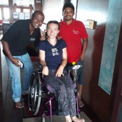 Liesl Hammer smiling in her wheelchair alongside two crew members aboard a boat, posing together in a friendly group photo.