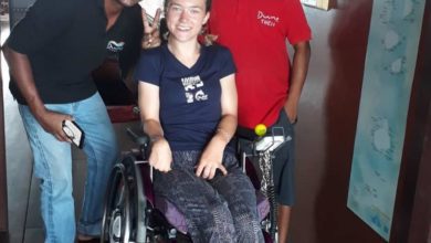Liesl Hammer smiling in her wheelchair alongside two crew members aboard a boat, posing together in a friendly group photo.