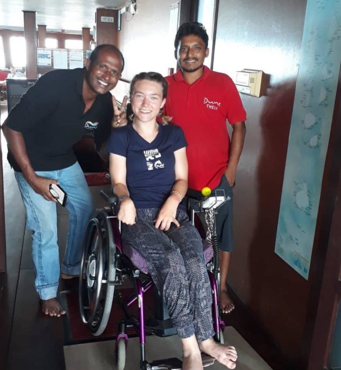 Liesl Hammer smiling in her wheelchair alongside two crew members aboard a boat, posing together in a friendly group photo.
